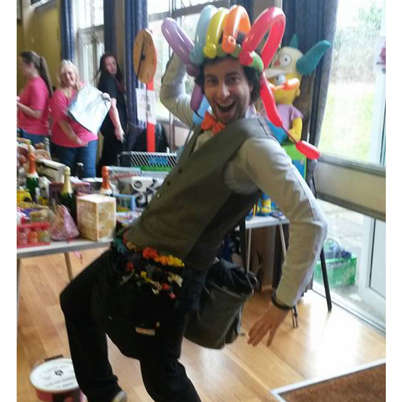 Guy, The Party Guy, wearing a hat made of balloons and pulling a fun pose